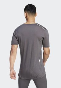 Szürke sport póló rövid ujjakkal, sima textúrával, lapos varrásokkal és kis logó címkével az alsó oldalon. A hátoldalon kerekített alsó szegély látható.