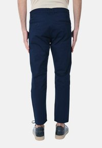 Pantaloni di cotone blu navy con vestibilità slim, dotati di tasche posteriori, dettagli cuciti e una texture liscia. Indossati con scarpe nere.