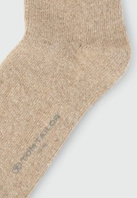Calcetín beige hecho de tejido de punto texturizado. Presenta una parte superior ligeramente acanalada y un logo impreso en gris en el lateral.