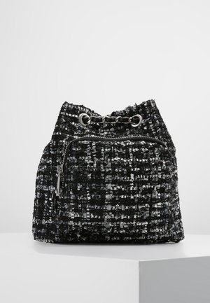 Czarnobiały plecak z tkaniny o fakturze, z ściągaczem i metalowymi oczkami, ozdobiony łańcuszkiem, z przednią kieszenią na zamek, pokazany na białym tle.