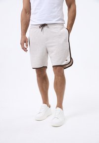 Shorts di cotone grigio chiaro con rifiniture marroni e accenti laterali, dotati di una vita elastica e un cordino, abbinati a sneaker bianche.
