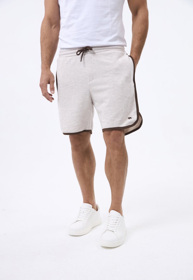 Shorts di cotone grigio chiaro con rifiniture marroni e accenti laterali, dotati di una vita elastica e un cordino, abbinati a sneaker bianche.