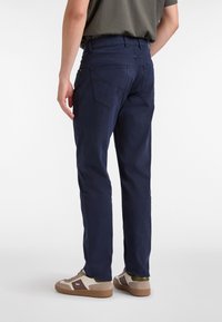 Pantalones azul marino de corte recto, con dos bolsillos traseros y una textura suave. Combinados con zapatillas de color claro.