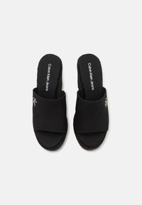 Sandalias de tela negra deslizantes con punta abierta y una tira ancha. Presentan detalles del logotipo en plata, plantilla texturizada y suela plana.