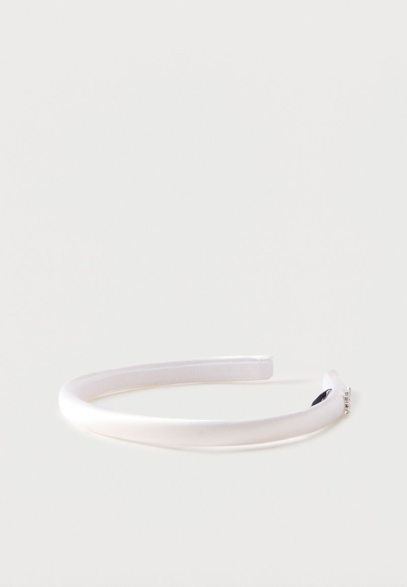 Λευκή μαλακή σατέν κορδέλα για το κεφάλι με μικρές στρας λεπτομέρειες στη μία άκρη, πάνω σε απλό ανοιχτό φόντο.