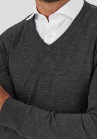 Pull à col en V gris foncé en maille douce, avec des manches longues et une coupe décontractée, superposé sur une chemise blanche à col.