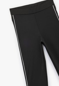 Sorte træningsleggings med bred talje, en glat overflade og hvide side-striber langs de ydre sømme.
