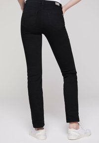 Jeans negros ajustados con una textura suave, que presentan dos bolsillos traseros y un detalle de costura mínimo, combinados con zapatillas blancas.