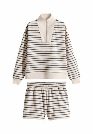 Beige og sort langærmet trøje med vandrette striber, halv lynlås og matchende elastiske shorts i taljen, lagt fladt på hvid baggrund.