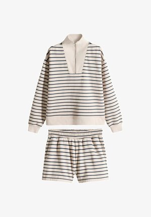 Pulover dugih rukava s horizontalnim prugama u bež i crnoj boji, s pola patentnim zatvaračem i odgovarajućim kratkim hlačama s elastičnim strukom, položen ravno na bijelu podlogu.