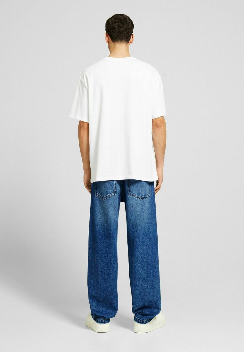 Camiseta de algodón blanca con mangas cortas, combinada con unos vaqueros de denim azul de corte holgado que tienen dos bolsillos traseros y una silueta recta.