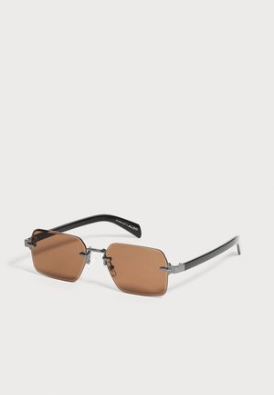 Lunettes de soleil rectangulaires teintées marron avec une fine monture métallique noire et des branches noires, reposant sur une surface blanche.