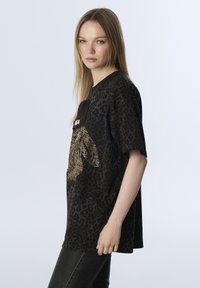 Schwarzes T-Shirt mit Leopardenmuster, das ein großes, strukturiertes Grafikdesign mit goldenen Akzenten zeigt. Kurzärmelig und mit lockerer Passform.