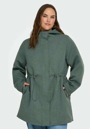 Zaļš kapucēts zamšādas jaka ar sašaurināmu jostasvīru, izgatavota no mīksta auduma, ar divām priekšējām kabatām un brīvu piegriezumu.