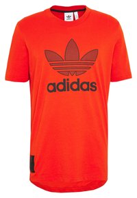 Červené bavlněné tričko s černým logem Adidas a ikonickými třemi pruhy. Krátké rukávy, kulatý výstřih a zakřivený lem se černým akcentem.