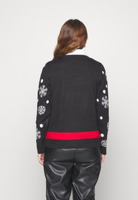 Svart tröja med vita snöflinge-mönster och ett röd horisontellt rand längst ner. Stickad tyg med avslappnad passform och långa ärmar.