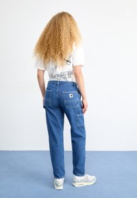 Light blue denim cargo pants with multiple pockets, a relaxed fit, and a small brand logo patch on the back. White t-shirt with graphic design.