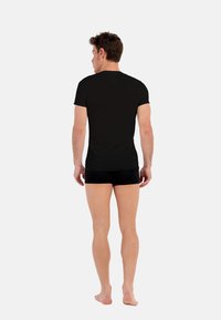 Czarny t-shirt z krótkim rękawem, wykonany z miękkiego materiału, dopasowany krój, gładka struktura, zestawiony z ciemnymi szortami, widok z tyłu.