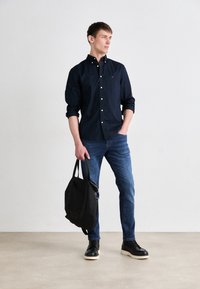 Laivastonsininen napitettava paita, siniset farkut, mustat saappaat ja musta käsilaukku. Paidassa on kaulus ja napit; farkut ovat slim-fit -malliset.