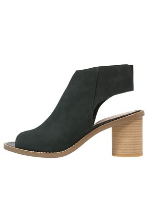 Sandale noire à talon ouvert avec une large bride à la cheville et un talon bloc beige empilé, vue de profil sur fond blanc.