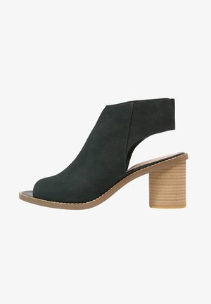 Sandale noire à talon ouvert avec une large bride à la cheville et un talon bloc beige empilé, vue de profil sur fond blanc.