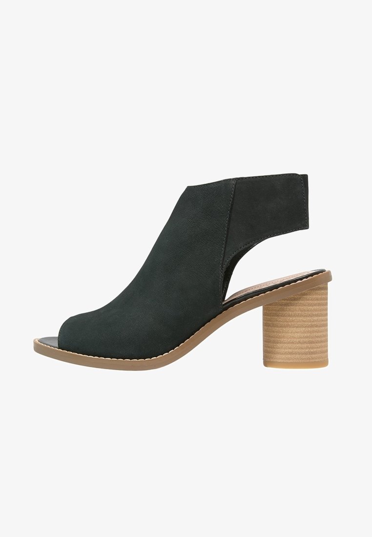 Sandale noire à talon ouvert avec une large bride à la cheville et un talon bloc beige empilé, vue de profil sur fond blanc.