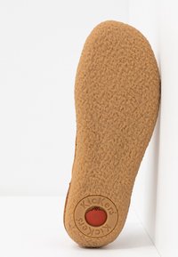 Semelle de chaussure en caoutchouc brun avec une surface texturée et un logo circulaire avec une pomme rouge au talon. Design plat et arrondi.