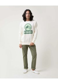 Sudadera de crema con gráfico verde "ALTONADOCK". Combinada con pantalones verde oliva y zapatillas blancas. Textura suave, corte relajado.