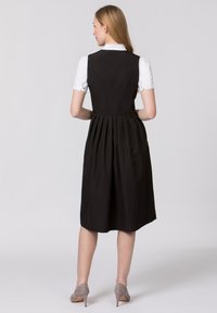 Black dress with pleated skirt, fitted bodice, and a white shirt detail at the collar. Features a smooth texture and knee-length design.