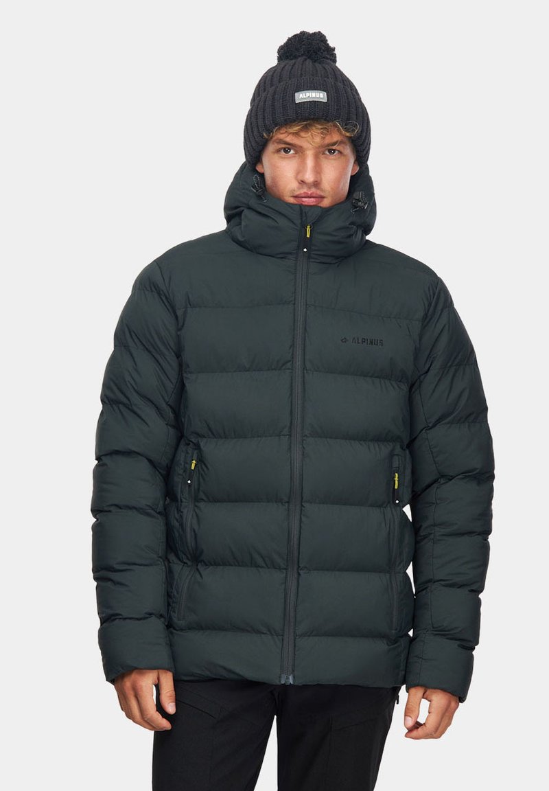 Ciemnozielona kurtka puchowa z wysokim kołnierzem, zamkiem z przodu i dwiema bocznymi kieszeniami. Brzegowa czarna czapka z logo spoczywa na głowie modela.
