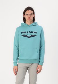 Turkusowy polar z kapturem wykonany z mieszanki bawełny, z przednią kieszenią typu pouch oraz czarnym nadrukowanym logo z motywem skrzydeł. Miękka faktura.