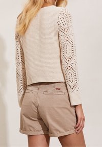 Virkat tröja i krämfärg med mönstrade långa ärmar, kombinerad med ljusbeige shorts med uppvikta fållar och bakfickor.