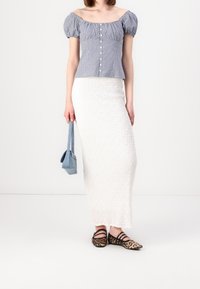 Top a spalla scoperta a quadri blu e bianchi con maniche a sbuffo, gonna bianca strutturata, ballerine con stampa leopardata e borsa blu piccola.