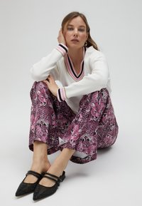 White long-sleeve top with pink and black striped neckline, paired with pink leopard-patterned wide-leg pants and black textured pointed-toe mules.