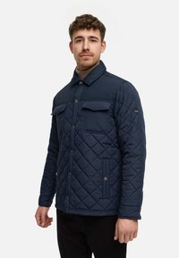 Giacca trapuntata blu navy con chiusura a bottoni, due tasche sul petto e tasche laterali. Presenta un colletto classico e un tessuto testurizzato.