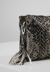 Borsa a tracolla in stampa pitone nero e grigio testurizzata, con cerniera argentata, accessori metallici e un dettaglio decorativo di nappina in pelle.