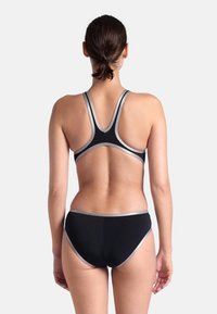 Conjunto de bañador negro que incluye un top tipo racerback y una parte inferior tipo bikini. Destacado con un ribete gris a lo largo de los bordes. Textura suave y diseño ajustado.