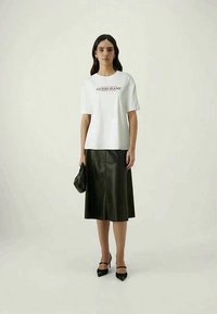 White cotton t-shirt with "GUESS JEANS" logo, paired with a black leather midi skirt, black heels, and a small black handbag. Simple design.