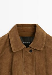 Veste en daim marron avec col pointu, fermeture à boutons noirs et étiquette "Massimo Dutti" visible à l'intérieur de l'encolure.
