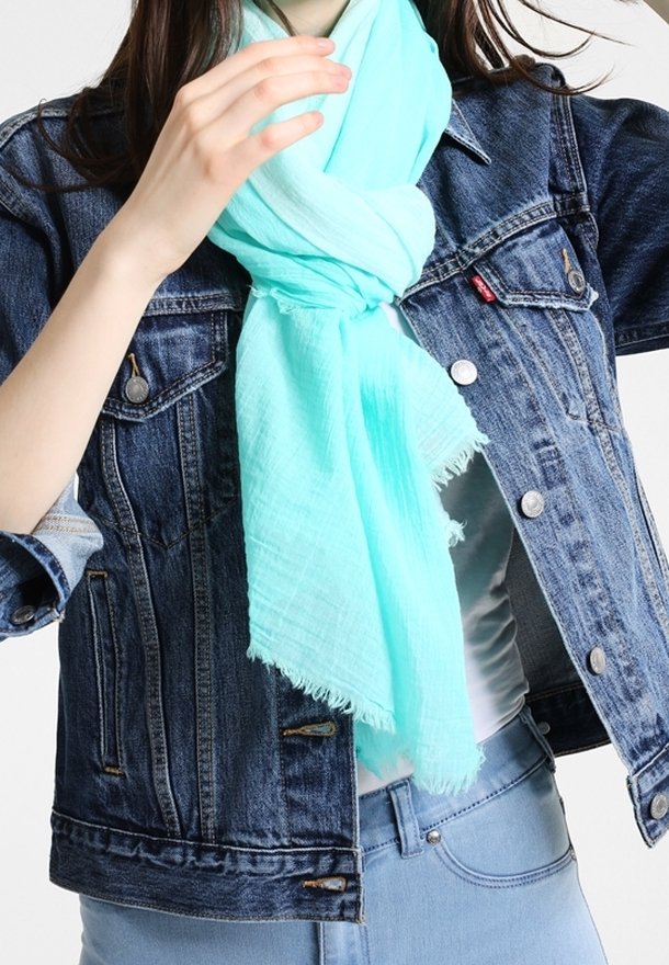 Personne portant une écharpe bleu clair nouée autour du cou et une veste en jean bleue par-dessus un haut blanc et un jean bleu clair.