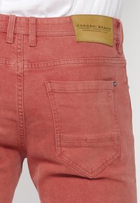 Jeans de mezclilla coral con corte recto, que presentan un parche de marca de cuero en la cinturilla y un bolsillo trasero rectangular.