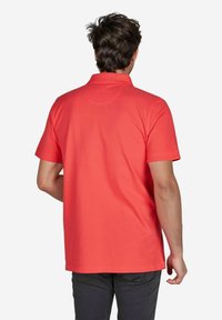 Korallefarbene Poloshirt mit kurzen Ärmeln und Kragen. Hergestellt aus Baumwolle, hat einen geraden Saum und dezente Stickdetails auf der Rückseite.