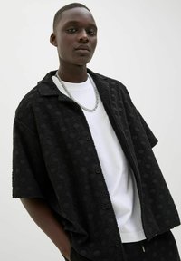 Black short-sleeve shirt with a textured wave pattern, button-down front, and a relaxed fit, layered over a white crew-neck t-shirt.