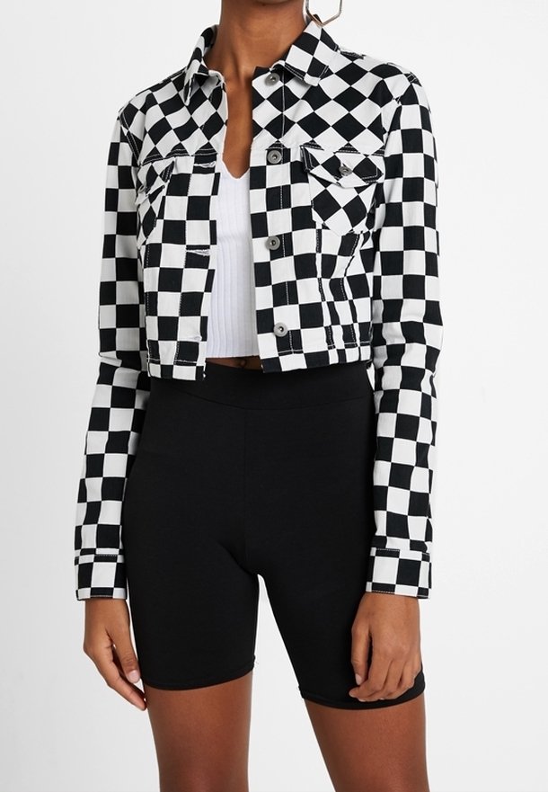 Avskuren svartvit rutig jacka som bärs över en vit ribbad crop top, i kombination med högmidjade svarta cykelshorts.