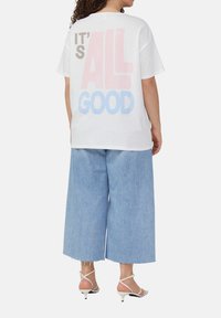 T-shirt en coton blanc avec un texte audacieux et coloré "C'EST TOUT BON" dans le dos. Associé à un pantalon en denim large bleu clair.
