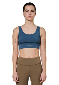 Sport BH i mørkeblå stof med brede stropper og en kant med "HALO" logo. Sammen med brune høj talje leggings. Glat tekstur.