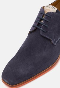 Scarpa da uomo in suede blu navy con punta quadrata, lacci e cuciture a contrasto. Suola in pelle marrone con una leggera lucentezza.