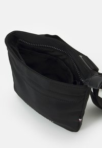 Borsa a tracolla in nylon nero con apertura superiore, dotata di una tasca con zip, tasca esterna piatta e tracolla regolabile. Texture liscia e opaca.
