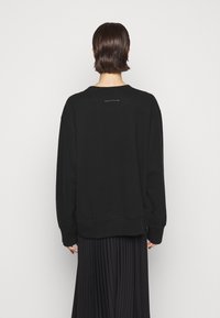 Černá mikina s kulatým výstřihem a dlouhými, volnými rukávy. Disponuje minimalistickým designem s jedním švem na zadní části.