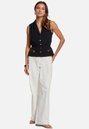 Blouse sans manches noire avec un décolleté en V, boutons sur le devant et taille peplum ; associé à un pantalon blanc à jambes larges et des sandales à lanières.